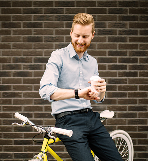 A young man leaning on a bicycle holding a coffee
